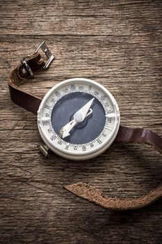 obsolete compass with leather strap on wooden table top in retro style