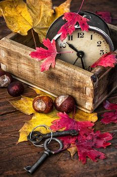 covered with autumn leaves old alarm clock in wooden box on the table