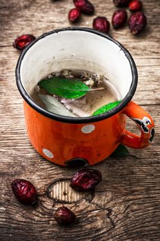 old iron mug of tea and dried berries of the wild rose on wooden table 