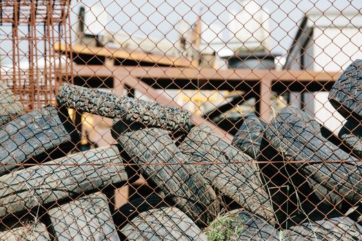 A pile of used car tyres waiting for recycle behind a rusted wire fence.