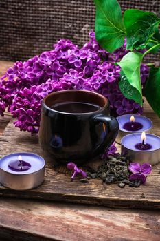 fragrant spring flower tea on the background of burning candles and lilac bouquet