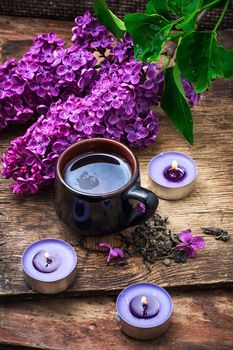 fragrant spring flower tea on the background of burning candles and lilac bouquet