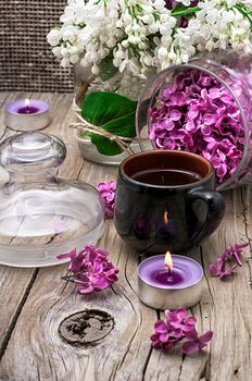 fragrant spring flower tea on the background of burning candles and lilac bouquet