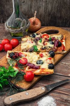 hunk of delicious meat pizza with bacon and olives on the background of the vegetables.The image is tinted