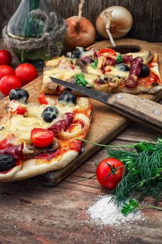 hunk of delicious meat pizza with bacon and olives on the background of the vegetables.The image is tinted