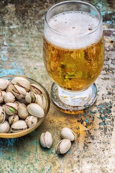 one glass glass of light beer with scattered on the table pistachios.Photo tinted