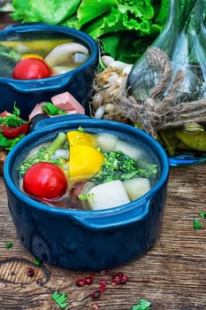 traditional soup of fresh vegetables in blue pot on wooden background