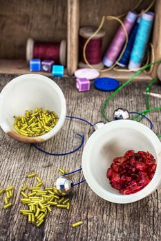 two vases with small beads on the background of tools for needlework.Selective focus.Photo tinted