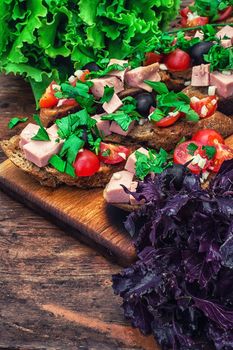 sandwiches with meat ,fresh tomatoes, onions and olives on wooden table top.Photo tinted