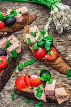 sandwiches with meat ,fresh tomatoes, onions and olives on wooden table top.Photo tinted.