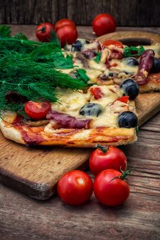 hunk of delicious meat pizza with bacon and olives on the background of the vegetables.The image is tinted