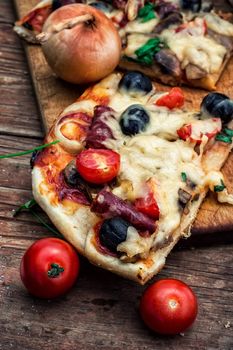 hunk of delicious meat pizza with bacon and olives on the background of the vegetables.The image is tinted