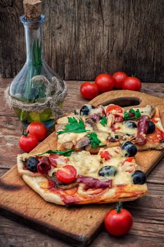 hunk of delicious meat pizza with bacon and olives on the background of the vegetables.The image is tinted
