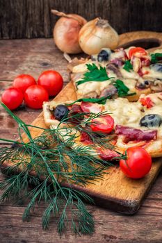 hunk of delicious meat pizza with bacon and olives on the background of the vegetables.The image is tinted
