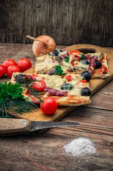 hunk of delicious meat pizza with bacon and olives on the background of the vegetables.The image is tinted