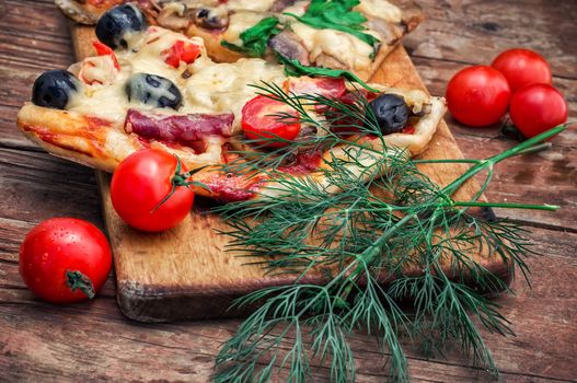 hunk of delicious meat pizza with bacon and olives on the background of the vegetables.The image is tinted