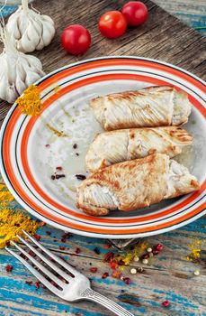 Turkey sausages roasted on round plate on wooden surface with tomatoes and spices.