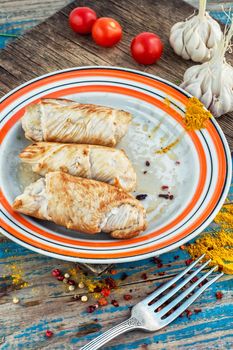 Turkey sausages roasted on round plate on wooden surface with tomatoes and spices.
