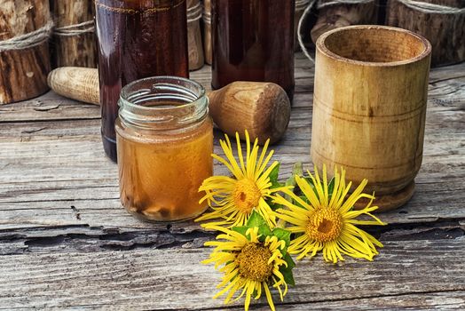 infusion of inflorescences and roots of the medicinal plant Inula on the wooden table next mortar and pestle.Photo tinted.