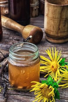 infusion of inflorescences and roots of the medicinal plant Inula on the wooden table next mortar and pestle.Photo tinted.Selective focus