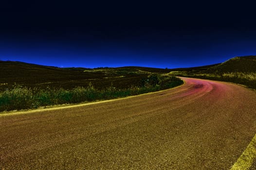 Winding Asphalt Road between Spring Plowed Fields of Sicily at Sunset