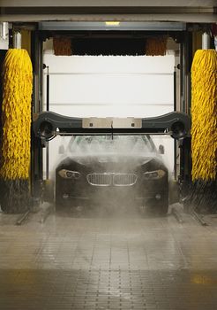 Black car spraying with water in station washing tunnel