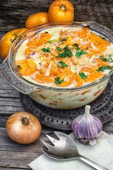 gratin of zucchini and yellow tomatoes on wooden background in glass bowl