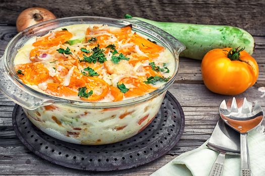 gratin of zucchini and yellow tomatoes on wooden background in glass bowl