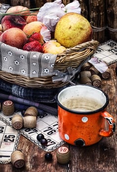 composition of the enamel cup with water on the background  fruit basket and Lotto games for picnic.Photo tinted.