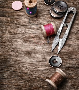 Scissors,thread and buttons on old wooden background.Photo tinted