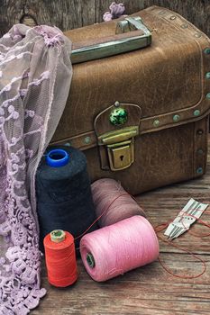spools of thread on background of old vintage suitcase with draped cloth with lace.Selective focus