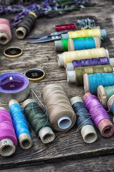 spools of thread on the old wooden background decorated with branches blossoming lavender.Selective focus
