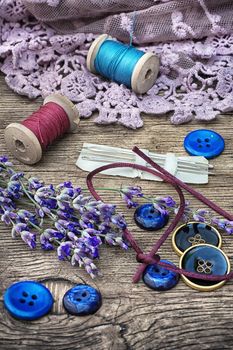 spools of thread on the old wooden background decorated with branches blossoming lavender.Selective focus