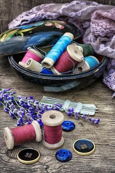 spools of thread on the old wooden background decorated with branches blossoming lavender.Selective focus