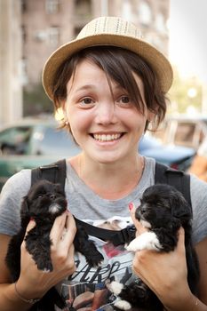 the young beautiful woman in a hat holds two little puppies in hand
