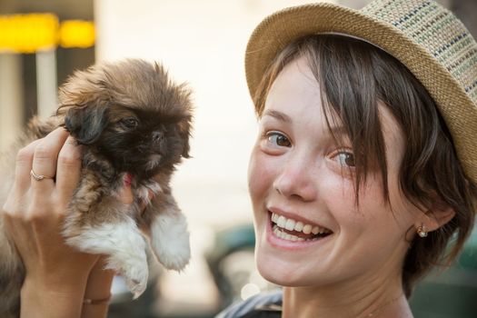 the young beautiful woman in a hat holds a little puppy in hand