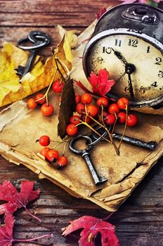 Od clock book and the keys on the wet table strewn with autumn leaves.Photo tinted.
