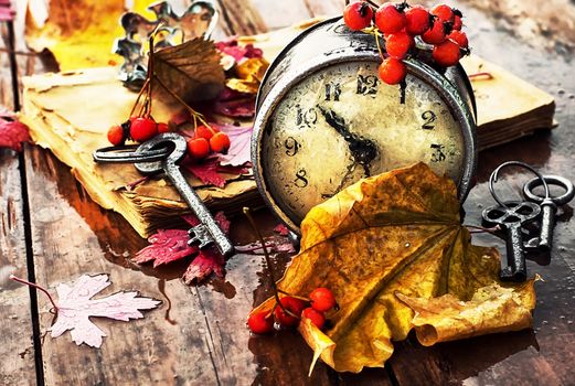 Od clock book and the keys on the wet table strewn with autumn leaves.Photo tinted.