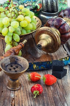 Old smoking  hookah and bunch of grapes on wooden surface.