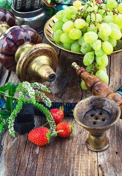 Old smoking  hookah and bunch of grapes on wooden surface.