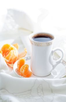Morning pleasure. Cup of black coffee and tangerine on bed