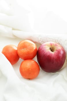 Good morning! Few tangerines and red apple on white textile