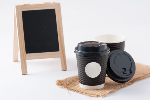Take away paper coffee cup with white sticker label for logo, text or message and small A-frame black board in blurry background