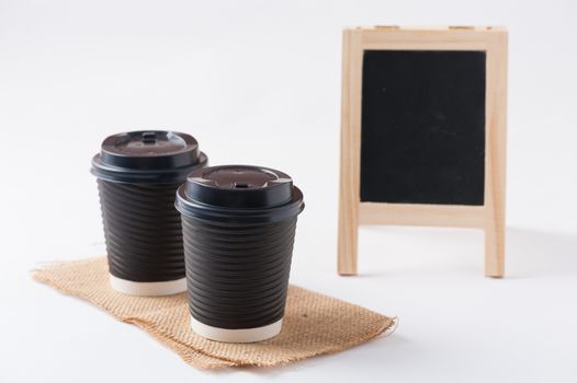 Take away paper coffee cup with small A-frame black board in blurry background
