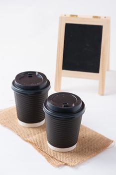 Take away paper coffee cup with small A-frame black board in blurry background