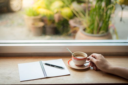 Male hand holding coffee cup on wood bar beside window at cafe in morning time