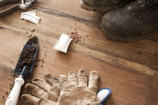 Gardening background concept with gloves , old boots and a trowel with scattered soil on a wooden surface with copy space, high angle view