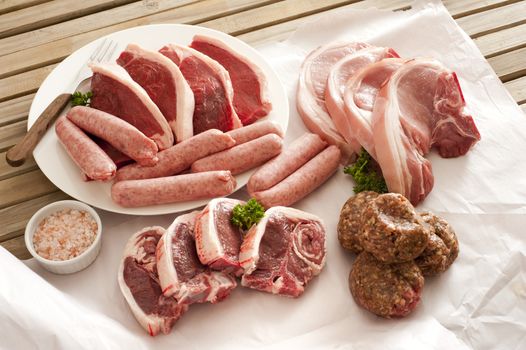 Assorted cuts of raw meat arranged on a wooden table with pork cutlets, beef steak, sausages, lamb chops and meatballs, or patties, high angle view