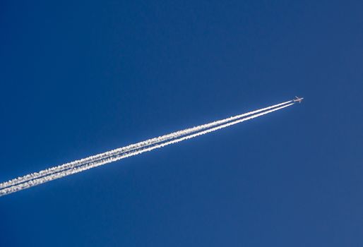 Aeroplane flying through clear blue sky with vapour trails