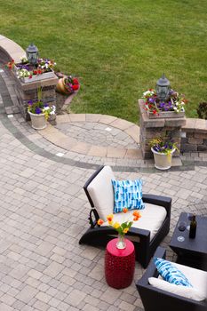 High Angle View of Luxury Patio with Outdoor Living Room Furniture and Stone Pillars Decorated with Colorful Flowers - Red Wine Served on Table near Comfortable Chairs on Stone Patio